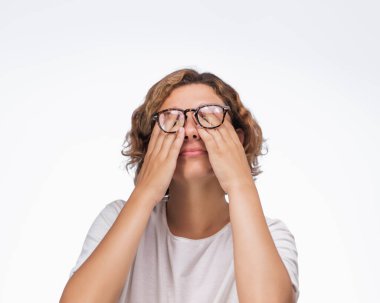 Gözlüklü yorgun bir kadın arka planda beyaz bir tişört giyerken gözlerini ovuşturuyor. Göz bakımı, yorgunluk, iş stresi ve sağlık ürünleri ile ilgili reklamlar için ideal