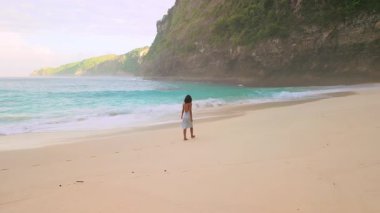 Huzurlu bir sabah ışığında Bali 'deki Kelingking Sahil Hattı boyunca yürüyen kadın, lüks seyahat, turizm ve sinematik yaşam tarzı temaları için iyi, tatil belleri için ideal, ilham