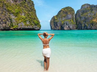 Tayland 'ın Maya Körfezi' nde yüksek kireçtaşı kayalıkları arasında berrak bir turkuaz denize bakan genç bir kadın. Konsept: seyahat yaşam tarzı, sağlık, yaz afişi, yüksek kaliteli reklam, turizm.