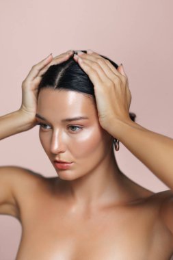 Işıl ışıl cildi ve parlak saçları olan, elleri kafasında pembe bir fonda poz veren güzel Latin bir kadın. Güzellik, cilt bakımı ya da kozmetik tanıtım temaları için mükemmel.