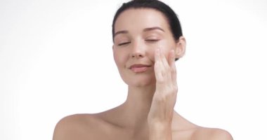 Çekici genç bir kadın sakin ve kendinden emin bir şekilde yanağına yaşlanma önleyici krem sürüyor. Cilt bakımı, kendine masaj ve temiz güzellik reklamı için ideal..
