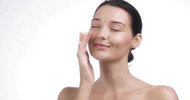 Mutlu beyaz kadın yüzüne nazikçe dokunuyor. Kapalı gözlerle ve yumuşak bir gülümsemeyle. Cilt bakımı reklamları, yüz kremi reklamları, kişisel bakım programları ve kozmetik dersleri için ideal..