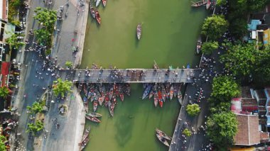 Yeşil nehrin üzerindeki Hoi An köprüsünün tepesinde, turistler ve demirlemiş teknelerle dolu. Seyahat reklamları, turizm tanıtımları, şehir taşımacılığı konseptleri ve Vietnam kültür hikayeleri için ideal..