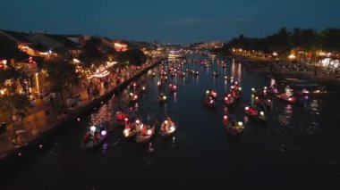 Gece fener festivali sırasında Hoi An nehrinin hızlı insansız hava aracı geçidi parlayan tekneleri, kalabalıkları ve şehir ışıklarını gösteriyor. Seyahat reklamları, kültürel medya veya gece manzarası temaları için harika.