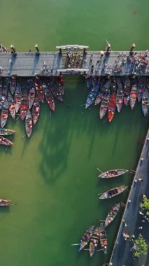 Hoi An Köprüsü 'nün tepeden aşağıya bakan insansız hava aracı manzarası. Aşağıda demirlemiş düzinelerce ahşap turist teknesi var. Yeşil nehir suyu ve yukarıdan geçen yayalar. Seyahat, turizm, Vietnam şehir yaşamı videoları için ideal.