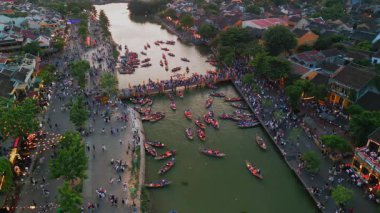 Hoi An 'ın ikonik Fener Köprüsü' nün ve gün batımında parlayan nehrin hava manzarası renkli tekneler ve hareketli kalabalıklarla dolu. Kültürel seyahat, turizm tanıtımları ve festival görüntüleri için ideal..
