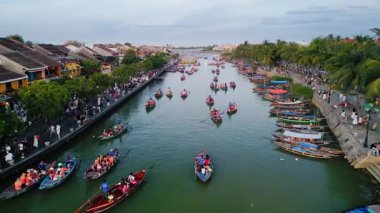 İHA görüntüleri Hoi An 'ın her iki taraftaki tekne ve kalabalıklarla dolu canlı nehrini yakalıyor. Turizm tanıtımları ve otantik Vietnam görselleri için yüksek kaliteli bir seyahat ve kültür sahnesi ideal.