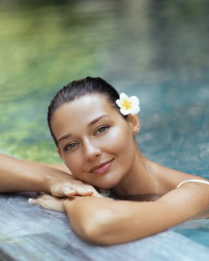 Saçında parlak bir ten ve çiçek olan güzel beyaz kadın havuz kenarında rahatlıyor, güzellik, sağlık, cilt bakımı, spa ve tropikal yaşam tarzı reklamları için konsept oluşturuyor..