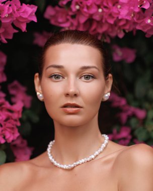 Parlak pembe bougainvillea çiçekleri çerçeveli inci takılar takan çarpıcı beyaz bir kadının yakın çekimi. Reklamlar, dergiler veya başyazılar için yüksek kaliteli moda ve güzellik kavramı.