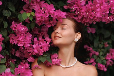 Duyusal güzellik portresi pembe bougainvillea çiçeklerine hafifçe dokunuyor, çıplak tenli kokulu çiçekler, parfüm reklamları için ideal, cilt bakımı, sağIık kavramları ve romantik yaşam tarzı görselleri..