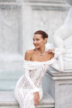 Beyaz dantelli bir elbise ve inci aksesuarlı gülümseyen kadın Vietnam 'ın Phu Quoc kentindeki bir çeşmenin mermer tabanında zarifçe oturuyor. Gelin yazıları, güzellik kampanyaları ya da seyahat promosyonları için mükemmel..
