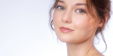 Parlak ciltli ve yumuşak makyajlı gülümseyen beyaz bir kadının yakın plan portresi. Güzellik, cilt bakımı, sağlık veya kozmetik reklamcılık ve tanıtım içeriği için mükemmel.