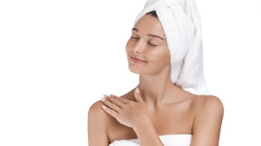 Parlak tenli barışçıl bir kadın kendini bir havluya sarar, gözlerini kapatır ve nazikçe gülümser. Rahatlamanın, güzelliğin vücut bulmuş hali, kendine özen göstermenin ve sağlığın tadını çıkarıyor..