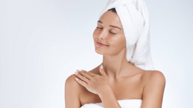 Işıl ışıl cildi olan sakin genç bir kadın, havluya sarılmış bir kişisel bakım anının tadını çıkarıyor. Kapalı gözleri ve yumuşak gülüşüyle güzellik, cilt bakımı ve sağlıklı bir ortamda vücut buluyor..