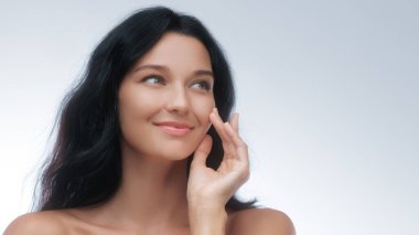 Güzel esmer kadın yanağına dokunurken hafifçe gülümsüyor. Parlak ve sağlıklı bir ten sergiliyor. Cilt bakımı, kozmetik ve güzellik tedavi reklamları için mükemmel..
