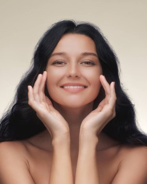 Mutlu esmer kadın onun pürüzsüz, parlak tenine dokunuyor, cilt bakımını, kaplıcayı ve güzellik tedavisini teşvik ediyor. Kozmetik, sağlık ve kişisel bakım reklamları için yüksek kaliteli portre.