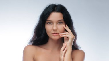 Yüzüne nazikçe dokunan kusursuz, parlak stüdyo ışıklarıyla yakalanmış zarif esmer kadın. Cilt bakımı, kozmetik, sağlık ve güzellik ürünleri promosyonları için ideal.