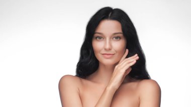 Yüzüne hafifçe dokunan pürüzsüz, parlak tenli beyaz bir kadın. Yüksek kaliteli stüdyo portresi cilt bakımı, kozmetik ürünleri, güzellik tedavileri veya sağlık reklamı için mükemmeldir..