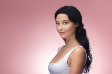 An elegant Asian woman with long black hair poses gracefully in a white tank top against a neutral background. Ideal for beauty, skincare, and fashion advertisements, highlighting natural elegance and