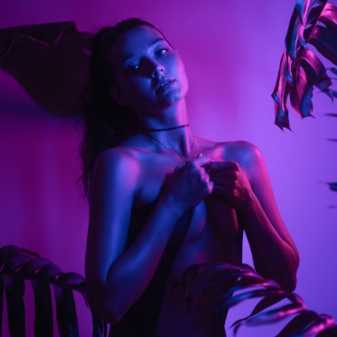 Genç Asyalı kadın karamsar stüdyo ışıklarında üstsüz poz veriyor neon mor ve mavi tonlarıyla. Moda, reklamcılık ya da yaratıcı promosyon kullanımı için mükemmel kaliteli kavramsal fotoğraf.