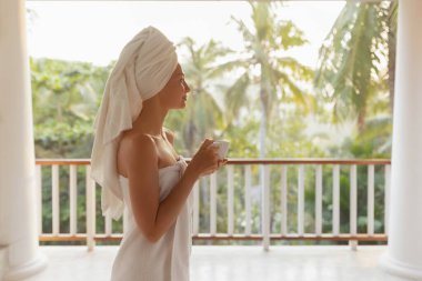 Sabah duşundan sonra, tropikal tatillerde elinde çay ya da kahveyle havluyla kaplıcaya giden kız. Muhteşem, rahatlatıcı kadının yan görüntüsü. Yüksek kalite fotoğraf