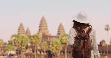 Güneş doğduğunda Kamboçya 'daki Angkor Wat tapınağına doğru yürüyen şapkalı ve sırt çantalı bir kadın turist. Macera seyahati, kültür turizmi, tanıtım ve yüksek kaliteli stok kullanımı için mükemmel.