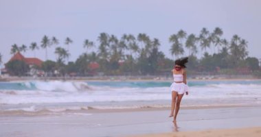 Sri Lanka 'daki Dickwella plajında yürüyen neşeli Asyalı kadın, seyahat ve yaşam tarzı içeriği için ideal, yaz tatili reklamları, turizm tanıtımı, özgürlük, varış ve refah temaları.