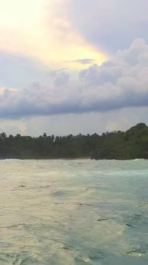 Yüksek hızlı insansız hava aracı videoları turkuaz okyanus dalgalarının altın bir günbatımı gökyüzünün altında tropik bir kıyıya vurduğunu gösteriyor. Seyahat, tanıtım, macera veya turizmle ilgili içerik için ideal.