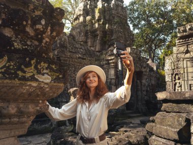 Angkor Wat Ta Som tapınağı seyahat konsepti, Kafkas kadın vlogger Siem Reap, Kamboçya 'da antik Khmer taş işçiliği yanında kompakt kamera ile selfie çekiyor, yüksek kaliteli kavramsal turizm imajı