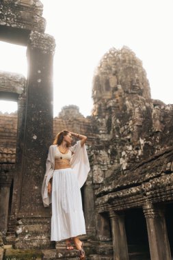 Beyaz boho kıyafetli kendine güvenen kadın Bayon Tapınağı 'ndaki Angkor Wat, Kamboçya' daki eski sütunların arasında çıplak ayakla duruyor. Gündoğumunda kaliteli seyahat, moda ve konsept fotoğraf.