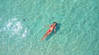 Deniz yıldızı sahilinin berrak turkuaz sularında yüzen kırmızı bikinili bir kadının hava görüntüsü, Phu Quoc Adası. Seyahat, yaşam tarzı ve plaj reklamları için kavramsal görüntüler.