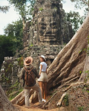 Kamboçya 'nın Angkor Wat sembolik Bayon Tapınağı kapısının önünde el ele tutuşan çok kültürlü bir çift. Turizm, romantizm veya keşif temaları için mükemmel kaliteli bir seyahat ve macera fotoğrafı.