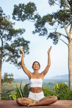 Huzurlu tropikal doğada kollarını kaldırarak yoga yapan kadın, refah reklamları, yaşam tarzı kampanyaları, seyahat pazarlaması, meditasyon rehberleri ve düşünceli olmak için ideal yüksek kalite kavramsal promosyon imajı.