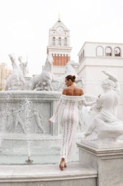 Beyaz dantelli kadın, Çeşme At 'ın yanından geçiyor. Saat Kulesi, Günbatımı Kasabası, Phu Quoc, Vietnam' da. Heykeller ve su spreyi ile..