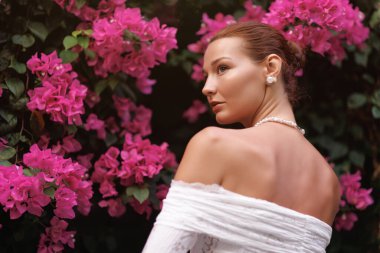Bougainvillea çiçekleri omuzları açık beyaz dantelli, inci kolyeli ve küpeli beyaz bir kadını çerçeveletip arkasına bakıyor. Moda reklamları için yüksek kaliteli güzellik konsepti. Romantik reklamlar için mükemmel..