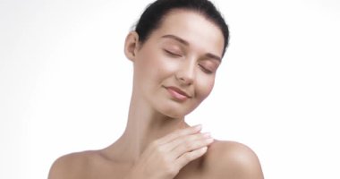 Beyaz bir stüdyoda gözleri kapalı poz verirken pürüzsüz, parlak tenli beyaz bir kadın yüzüne hafifçe dokunuyor. Kozmetik, sağlık ve kaplıca kampanyaları için mükemmel güzellik ve cilt tanıtımı.