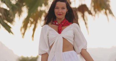 Esmer kadın kameraya doğru eğilmiş, beyaz bir gülümseme ve palmiye çizgili bir otelde kırmızı bir eşarp takıyor. Güzellik reklamları, seyahat pazarlaması, romantik yaşam tarzı ve sosyal etkinlikler için mükemmel..