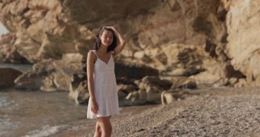 Romantik çift sıcak güneş ışığı altında tenha bir çakıl taşlı plajda tanışır, sonra el ele tutuşur ve uçurumların kenarında yürür. Flört reklamları, balayı tanıtımları, seyahat markaları ve sinematik aşk hikayeleri için ideal..