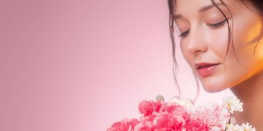 Pembe arka planda pembe karanfil buketinin yanında gözleri kapalı bir kadın profili. Yumuşak stüdyo ışığı ve fotokopi alanı, cilt reklamları, afişler ve çevrimiçi ambalaj için ideal.