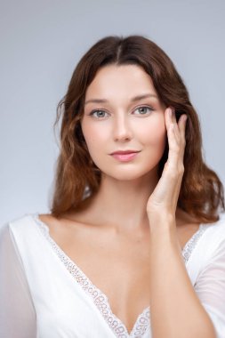 Zarif, parlak ciltli ve saçı açık genç bir kadın yüzüne hafifçe dokunuyor. Yüksek kalite cilt bakımı ve güzellik portresi, spa, sağlık, kozmetik, moda, tanıtım ve reklam tasarımı için mükemmel..