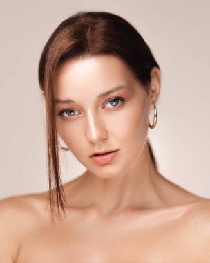 Parlak cilt ve çıplak makyajlı, büyük halka küpeler takan şık bir genç kadının yakın plan portresi. Güzellik malzemeleri, cilt bakımı reklamları ya da üst düzey kozmetik ürünler tanıtımı için ideal..