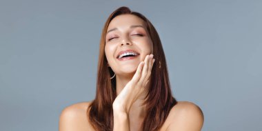 Beyaz tenli ve doğal makyajlı beyaz bir kadın bir güzellik konsepti çekiminde yüzüne dokunurken neşeyle gülüyor. Cilt bakımı, sağlık ve kozmetik mutluluk temalı reklamlar için ideal..