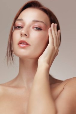 Parlak tenli, yumuşak şeftali makyajlı ve nazikçe yanağına dokunan genç bir kadının dikey çekimleri. Lüks cilt bakımı, sağlık ve kozmetik reklam malzemeleri için mükemmel..