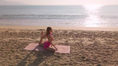 Pembe spor giysili zayıf kadın Vietnam 'da Da Nang' da deniz kenarında yoga pozları veriyor. Huzurlu gündoğumu ve nazik dalgalar refah ve seyahat temaları için ideal bir sahne yaratır..