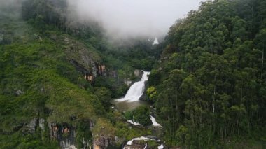 Bomburu Ella Şelalesi 'nin Nuwara Eliya, Sri Lanka yakınlarındaki hava manzarası bulutlar geçerken yemyeşil uçurumlardan aşağı dökülüyor. Destansı doğal ruh hali, turizm pazarlaması, reklamlar ve belgesel görüntüleri için mükemmel..