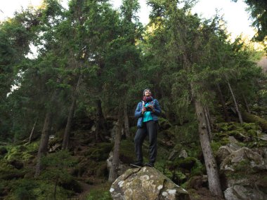 Kadın fotoğrafçı, Evergreen Ormanı 'nda yosunlu kayanın üzerinde duruyor, elinde kamerayla yukarı bakıyor. Doğal açık hava sahnesi, seyahat reklamları, bloglar, web afişleri ve yayın kampanyaları için ideal..