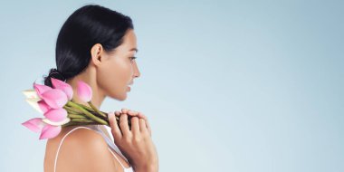 Elinde pembe nilüfer çiçekleri tutan, temiz mavi arkaplan ve kopyalama alanı olan güzel bir kadının yan profili. Parfüm, cilt bakımı, kozmetik, kaplıca ya da sağlık reklamları için ideal yüksek kalite kavramsal portre.