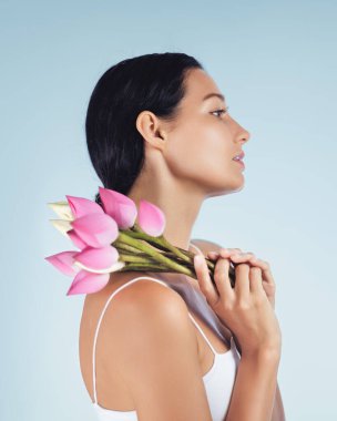 Omzunda pembe nilüfer tomurcukları tutan zarif bir kadının profili doğal güzellik ve sağlığını gösteriyor. Spa tedavileri, lüks cilt ürünleri ve güzellik için mükemmel.