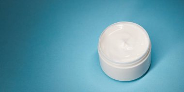 Mavi zemin üzerinde açık nemlendirici krem kavanozu geniş fotokopi alanı, temiz stüdyo ışıkları ve yumuşak gölgesi var. Cilt bakımı reklamları, web sitesi başlıkları, ambalaj modelleri, ekommerce ve sosyal paylaşımlar için ideal.