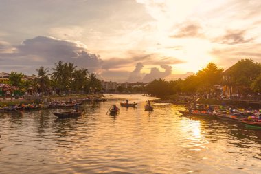 Fener yanan tekneler Hoi Nehri 'nde yüzüyor altın saatinde parlak gökyüzü ve siluetlerle. Turizm reklamları, manzaralı Güneydoğu Asya içeriği veya barışçıl doğa görselleri için harika.